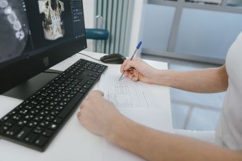 Close-up of a healthcare worker analysing x-ray results and taking notes on a computer desk.