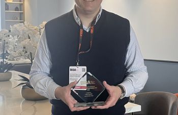 A standing Dr Roesch is shown smiling at the camera and holding his award from BISA in an informal setting which could be his living room.