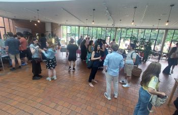 A photograph of students mingling at the evening reception in the ACCA cafe. They are enjoying refreshments, talking and enjoying themselves.