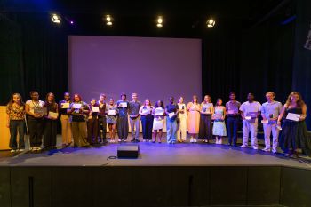 A photograph of around 20 students standing on the Attenborough Centre stage, holding the awards they received on the night.