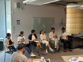 Six panellists sit in a row at the front of a seminar room during a discussion, with audience members seated in the foreground.