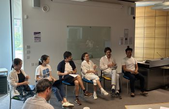 Six panellists sit in a row at the front of a seminar room during a discussion, with audience members seated in the foreground.