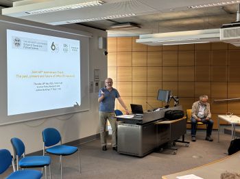 presenter stands at a lectern in a University of Sussex lecture room beside a projected slide for the “Joint 60th Anniversary Event: The past, present and future of SPRU-STIS Research
