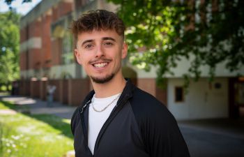 Morgan Page smiling at the camera, he is standing outside at the University of Sussex.