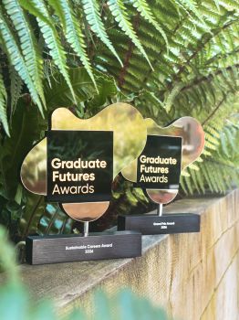 A photo of the two award trophies, which are gold and black, with the titles 'Sustainable Careers Award' and 'Grand Prix Award' printed along the bottom. They are photographed on a ledge, with leaves in the background.