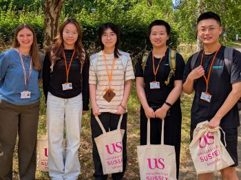 Group of international students with Sussex bags under a tree