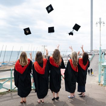 University of Sussex students throw mortarboard caps in the air celebrating graduation.