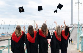 University of Sussex students throw mortarboard caps in the air celebrating graduation.