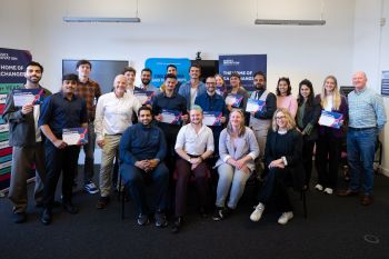 A group of people - comprised of this year's Momentum Incubator participants, and members of Sussex's Careers and Entrepreneurship team and the Sussex Innovation team - are photographed smiling at the camera, shot inside of a room at Sussex Innovation
