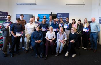 A group of people - comprised of this year's Momentum Incubator participants, and members of Sussex's Careers and Entrepreneurship team and the Sussex Innovation team - are photographed smiling at the camera, shot inside of a room at Sussex Innovation