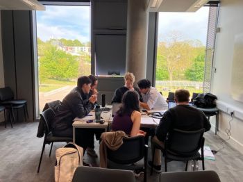 Group of male and female students sat at a classroom table doing joint work on AI