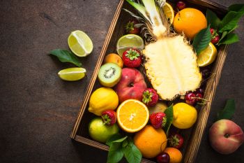 Fruit and berries in wooden box over dark stone table. Top view with copy space.  Pineapple, citrus and berry mix.