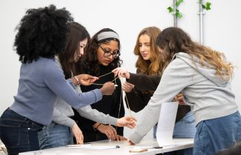A photo of students working on building a structure on a table, as part of a team-building task