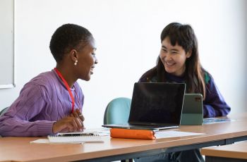 Two smiling researchers chat to each other over laptops.