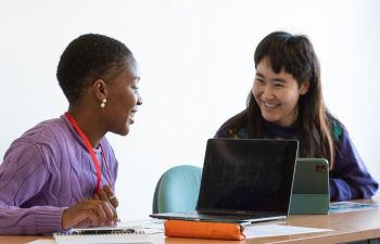 Two smiling researchers chat to each other over laptops.