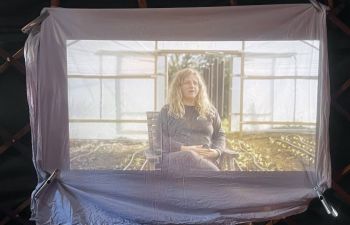 Image of a woman sitting in a greenhouse, projected onto a large fabric screen inside a dark tent.