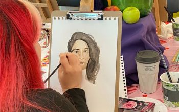 A student with dyed hair painting a portrait of someone