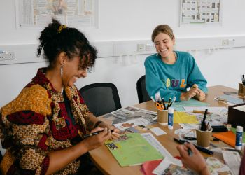 Participants sit around a table cutting, drawing and working with collage materials during a creative zine-making activity.