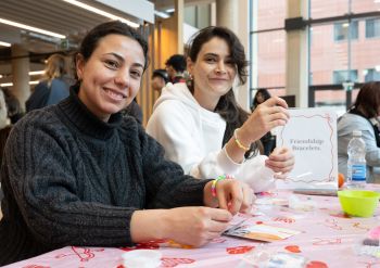 Two students smiling at the camera wearing friendship bracelets they've made