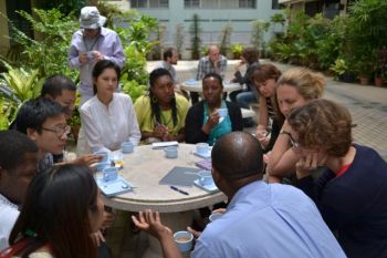 A group of people sat around a table talking, drinking tea and taking notes