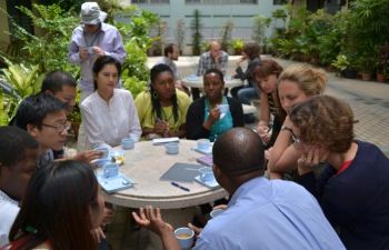 A group of people sat around a table talking, drinking tea and taking notes