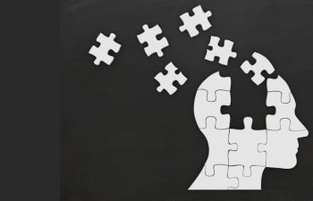 A white silhouette head with jigsaw pieces flying out of it on a black background