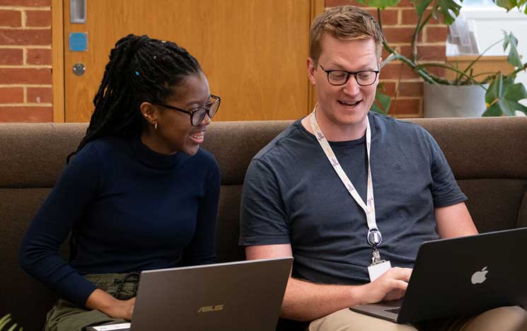 Two students with laptops, chatting and smiling