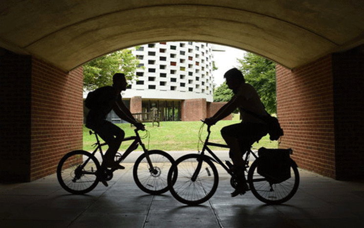 two people on bikes cycle on campus