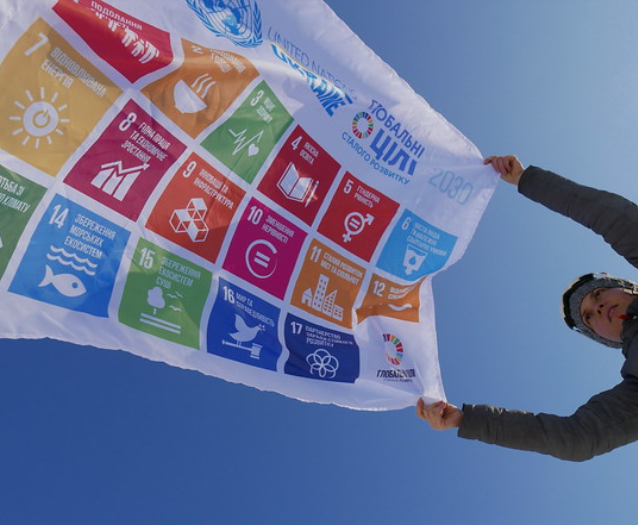Someone flying a flag with the United Nations sustainable development goals with a blue sky in the background.