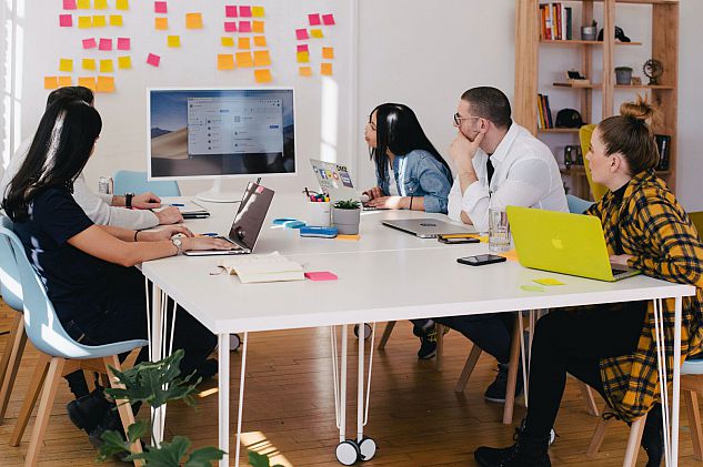 Group of people around a desk look at a creative wall planner