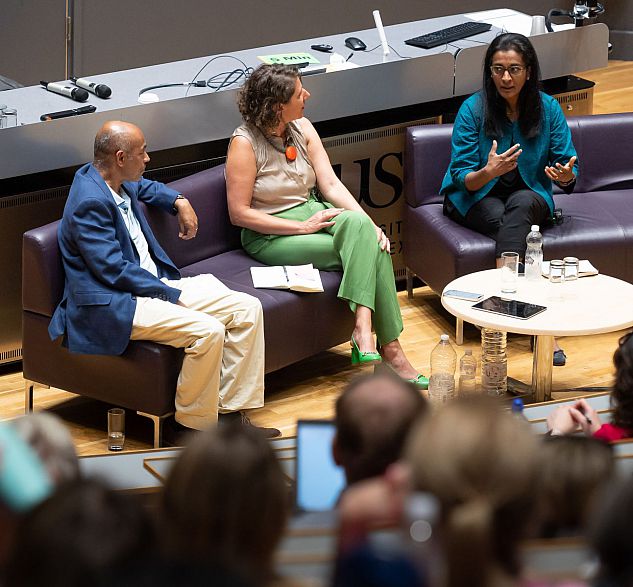 Chair in conversation with speakers of BAM2023 Day Three Plenary at front of large lecture hall