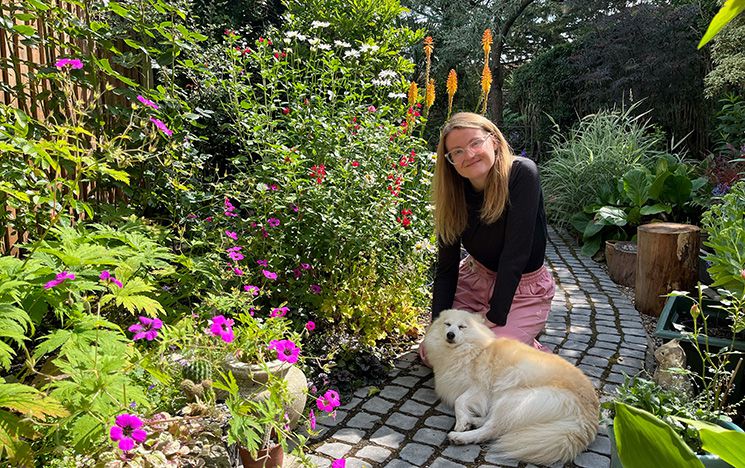 Phillipa Groome sat in a garden with flowers and a dog