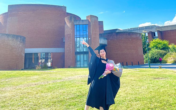 Manni Li celebrating in her graduation gown outside ACCA holding flowers in the sunshine