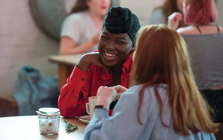 A mentor and mentee having a friendly chat an coffee in a café, smiling.