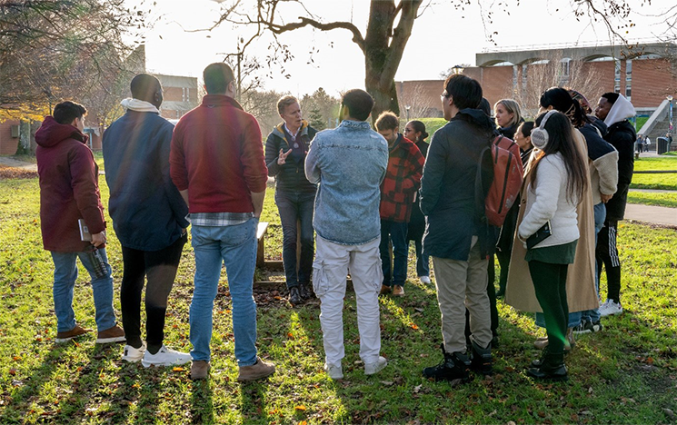A group of students gathered round a lecturer on the grass outside the library.