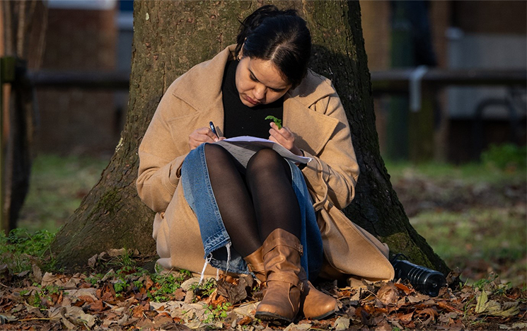 A student sitting on the ground against a tree studying.