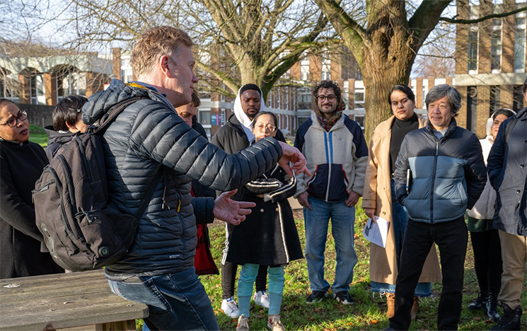 A group of students listening to a lecturer outside a university building.