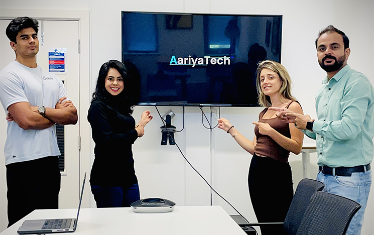A photo of the AariyaTech UK Team, in an office, standing around a screen looking at the camera