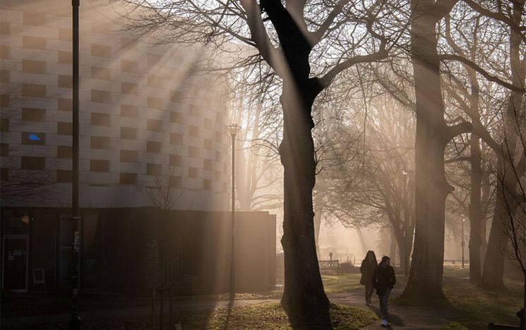 Sun shines through the mist whilst students walk past the Meeting House