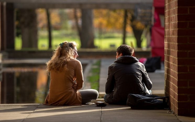 Two students sit by the moat in the courtyard of Falmer House