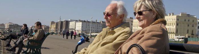 oloder man and woman sitting together smiling on a bench on the seafront