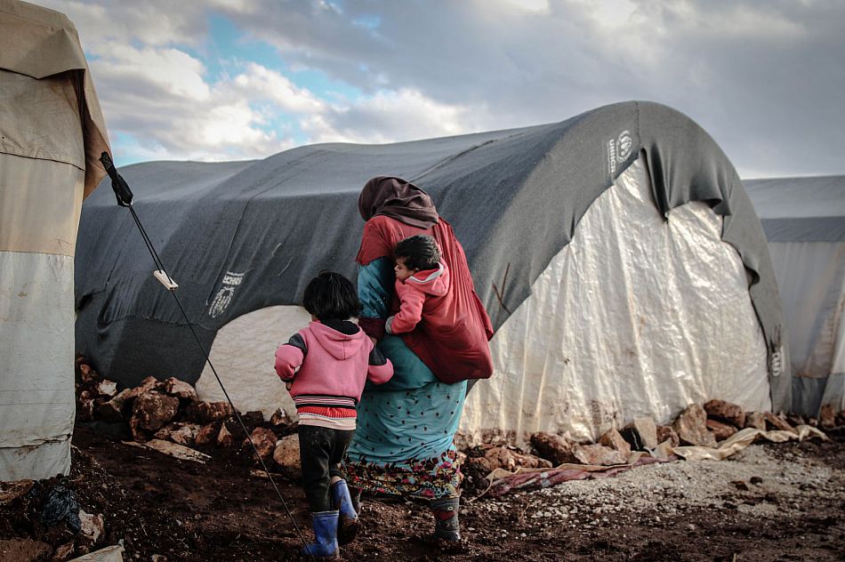 a refugee walking with two small children towards a large tent