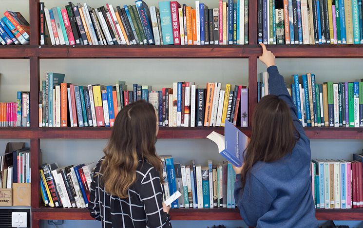 Two people look at books on a shelf in a library