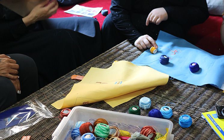 Women in Shatila Camp, Lebanon. Hands reaching to threads on a table.