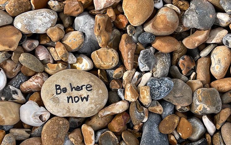 Pebbles on Brighton beach, one pebble has 'be here now' written on it