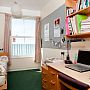 Photo of the inside of a bedroom in a Kings Road flat, showing a comfortable room with single bed, pinboard, study desk with draws and bookshelves, and a window with a stunning sea view.