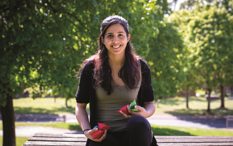 Shobita sitting on a bench on a sunny day smiling and holding small beanbags
