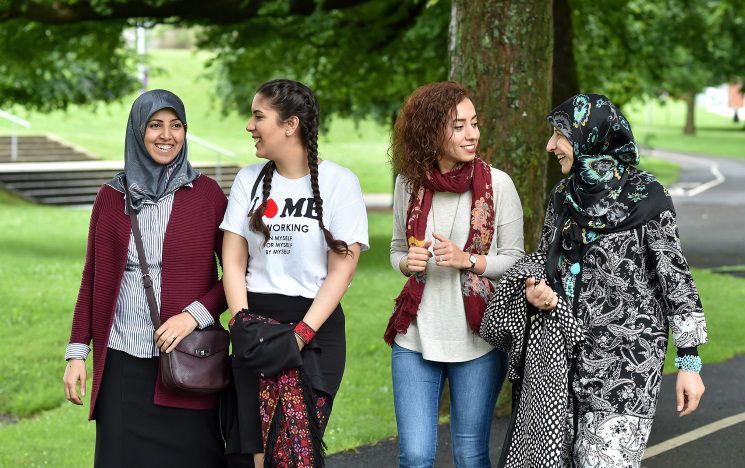 Four Egyptian students walking through a very green campus chatting and laughing