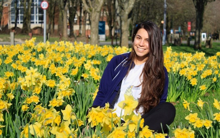 a student sits in a bed of flowers smiling