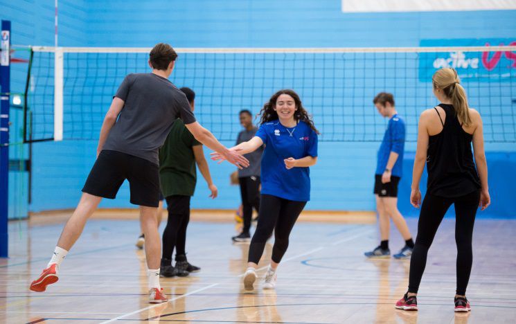 Students playing volleyball indoors high fiving and smiling